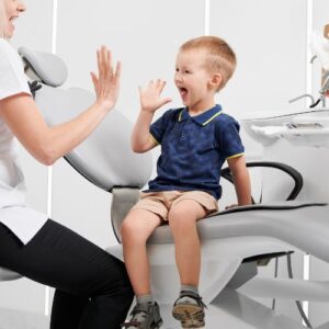 Prima visita, bimbo seduto su poltrona dentista che da il cinque a pedodonzista